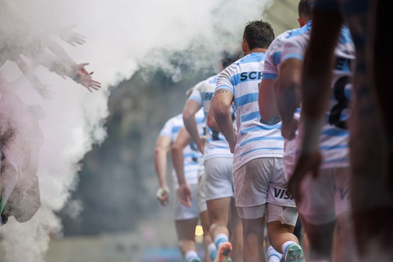 A rugby team walks out through smoke onto the pitch